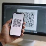 main tenant smartphone devant ecran pc affichant qr code
